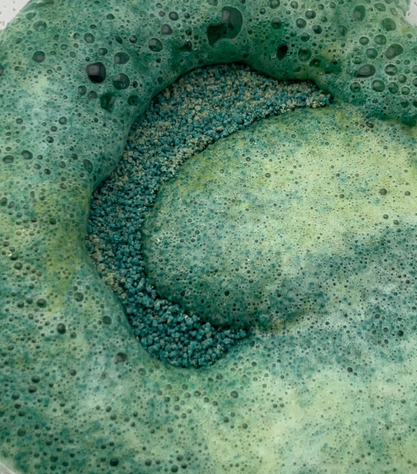 Close-up of a green potion powder beginning to fizz and foam after water is poured on