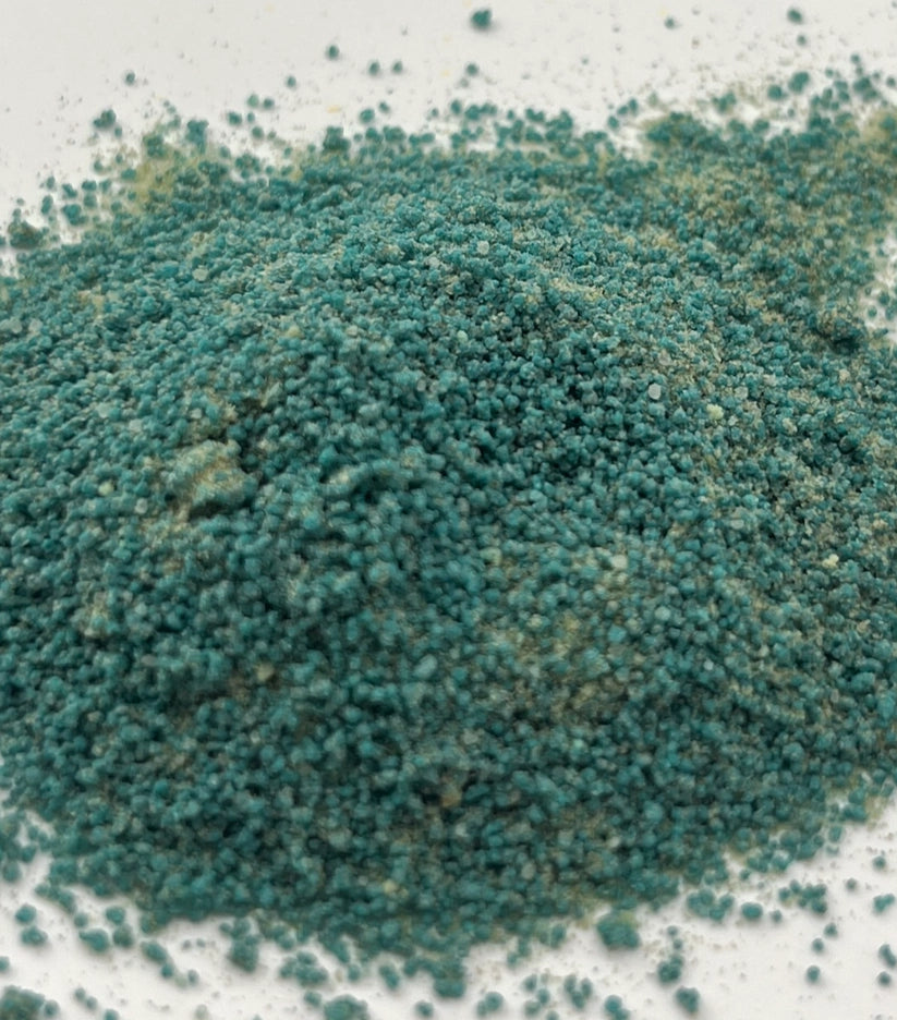 Close-up of blue-green potion powder that has a sand-like texture on a white background