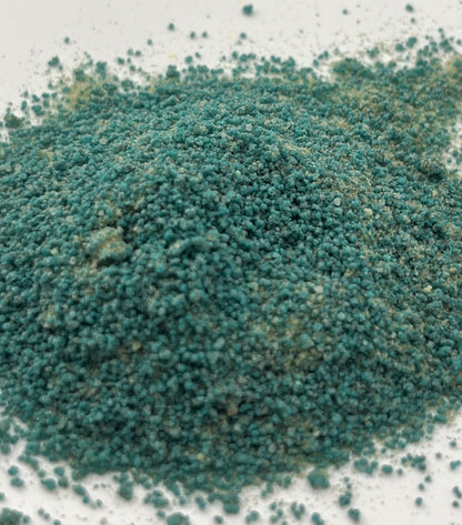Close-up of blue-green potion powder that has a sand-like texture on a white background