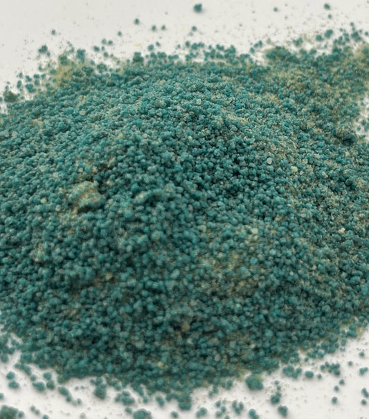 Close-up of blue-green potion powder that has a sand-like texture on a white background