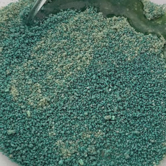 A Video showing green potion powder which has a sand like texture having water dropped on to it and it fizzing and foaming to make green bubbles