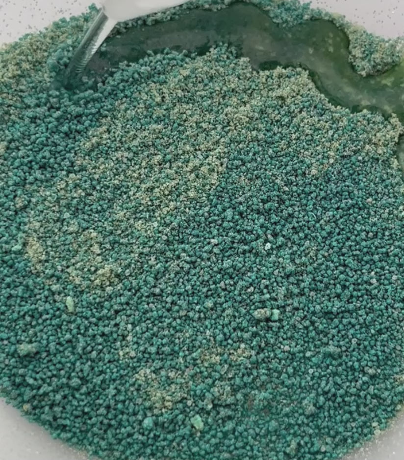 A Video showing green potion powder which has a sand like texture having water dropped on to it and it fizzing and foaming to make green bubbles